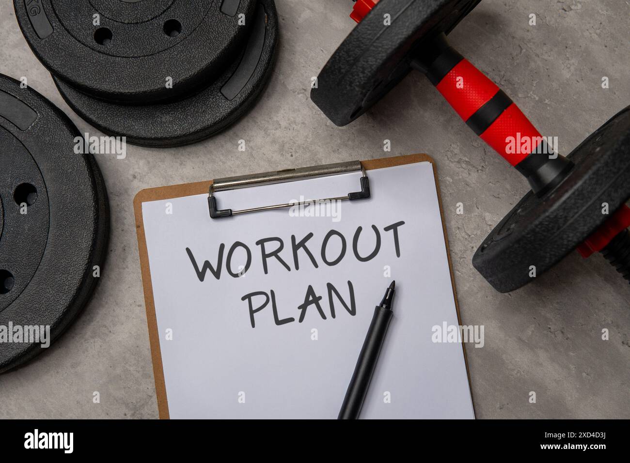 Ein Nahbild eines Clipboards mit einem TRAININGSPLAN, der neben einer schwarzen Hantel und Gewichtsplatten steht. Sport- und Fitnesskonzept. Stockfoto