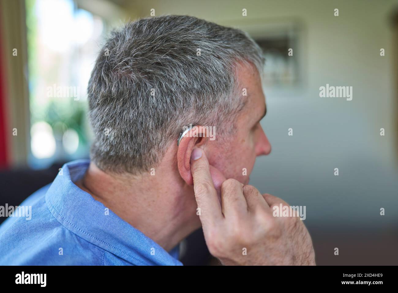 Nahaufnahme Von Reifem Mann, Der Zu Hause Ein Schnurloses Hörgerät Einsetzt Stockfoto