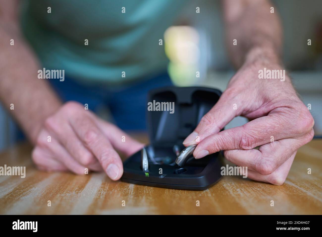 Nahaufnahme Eines Mannes, Der Zu Hause Ein Drahtloses Hörgerät Oder Gerät Aus Der Ladetasche Nimmt Stockfoto