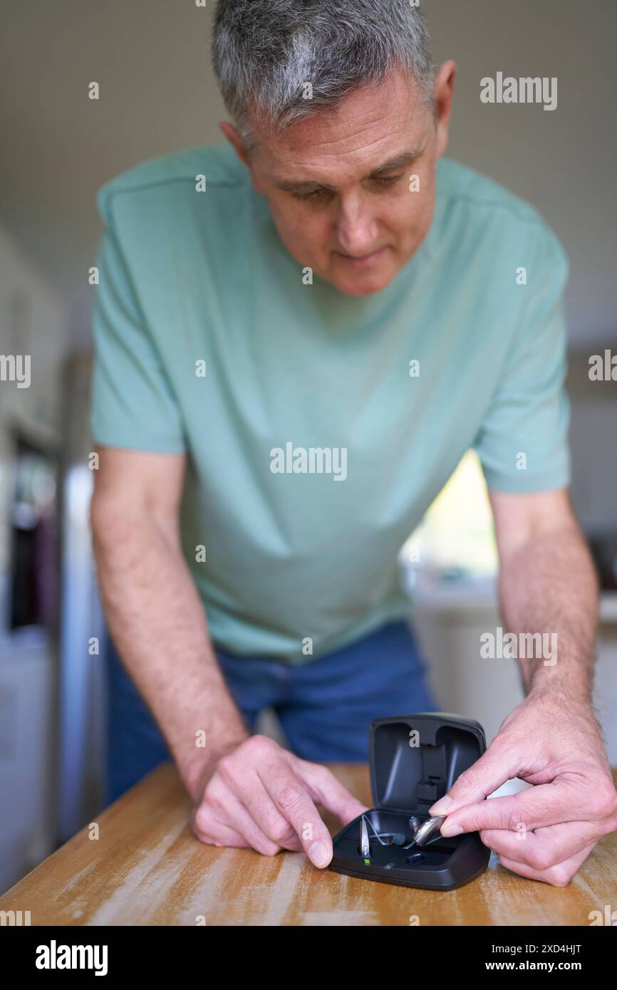 Reifer Mann, Der Zu Hause Ein Schnurloses Hörgerät Oder Ein Gerät Aus Der Ladetasche Nimmt Stockfoto