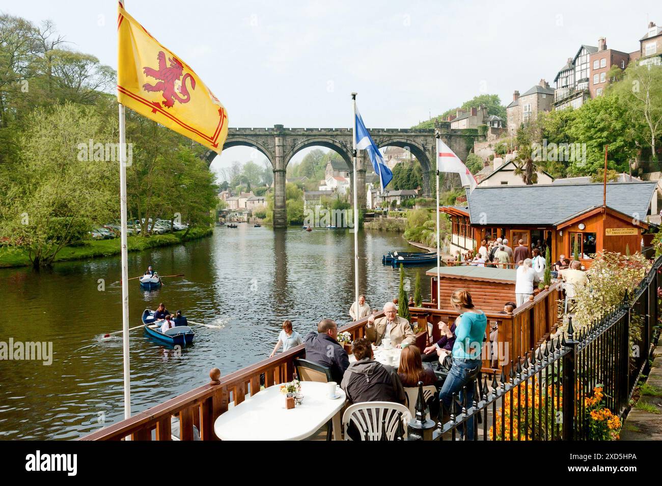 Touristen genießen Speisen und Getränke und beobachten Boote, die an einem sonnigen Nachmittag auf dem Fluss Nidd in Knaresborough, Yorkshire, rudern Stockfoto