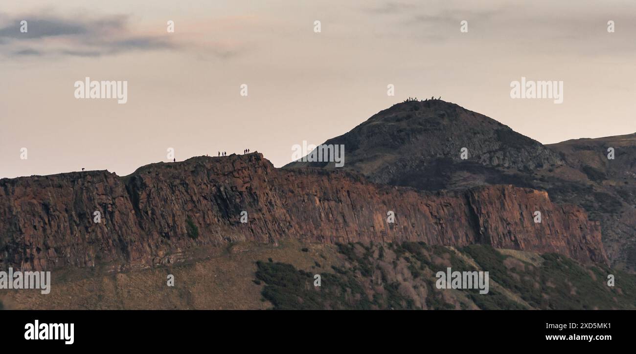 Panoramablick auf die Salisbury Crags in Edinburgh mit Menschen, die am Rand der Klippe und dem Gipfel von Arthurs sitzen dahinter Stockfoto