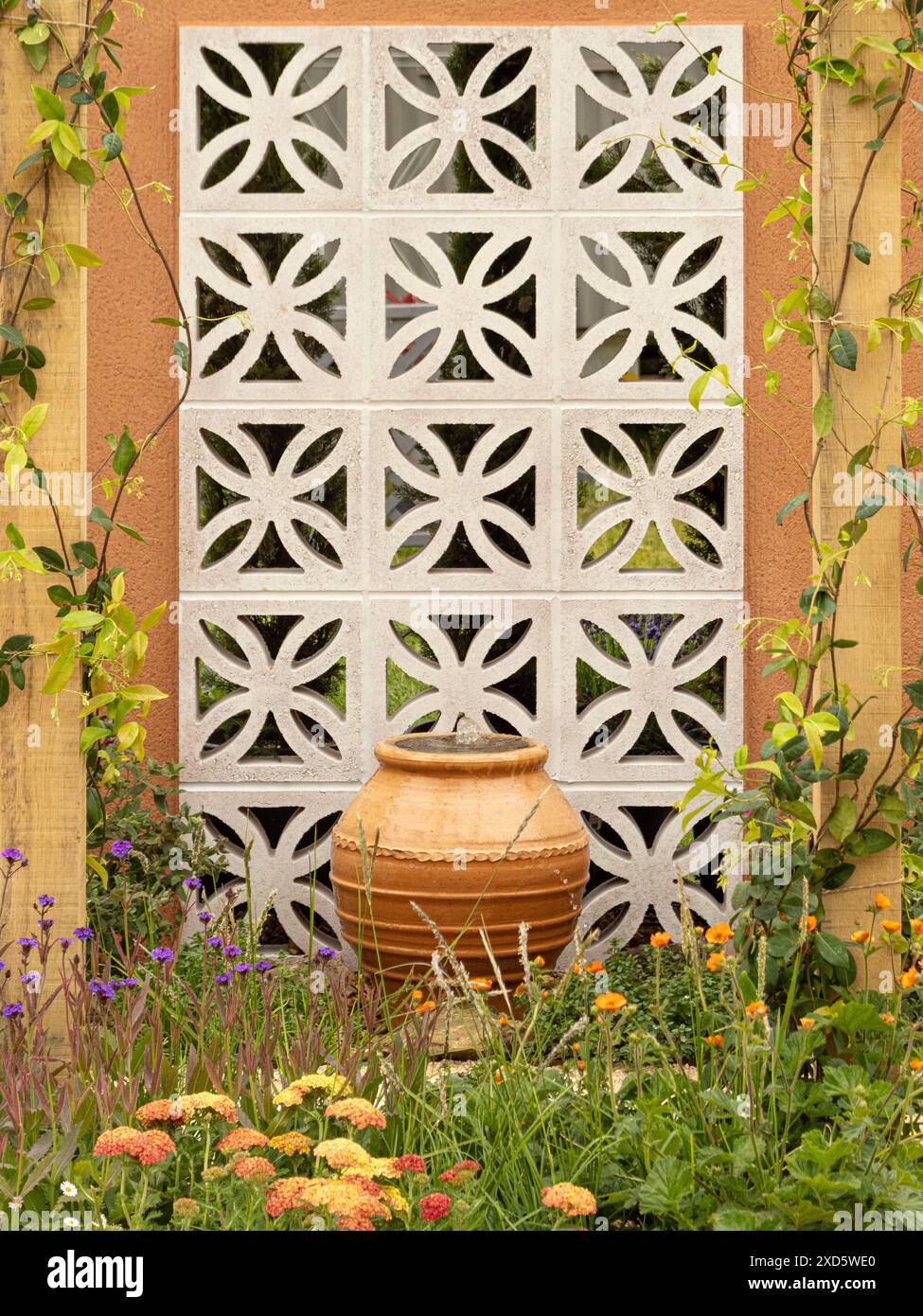 Terrakotta-Urnen-Wasserspiel, das an einer dekorativen Blockwand in einem britischen Garten mit orangefarbenen Blüten im Vordergrund steht Stockfoto