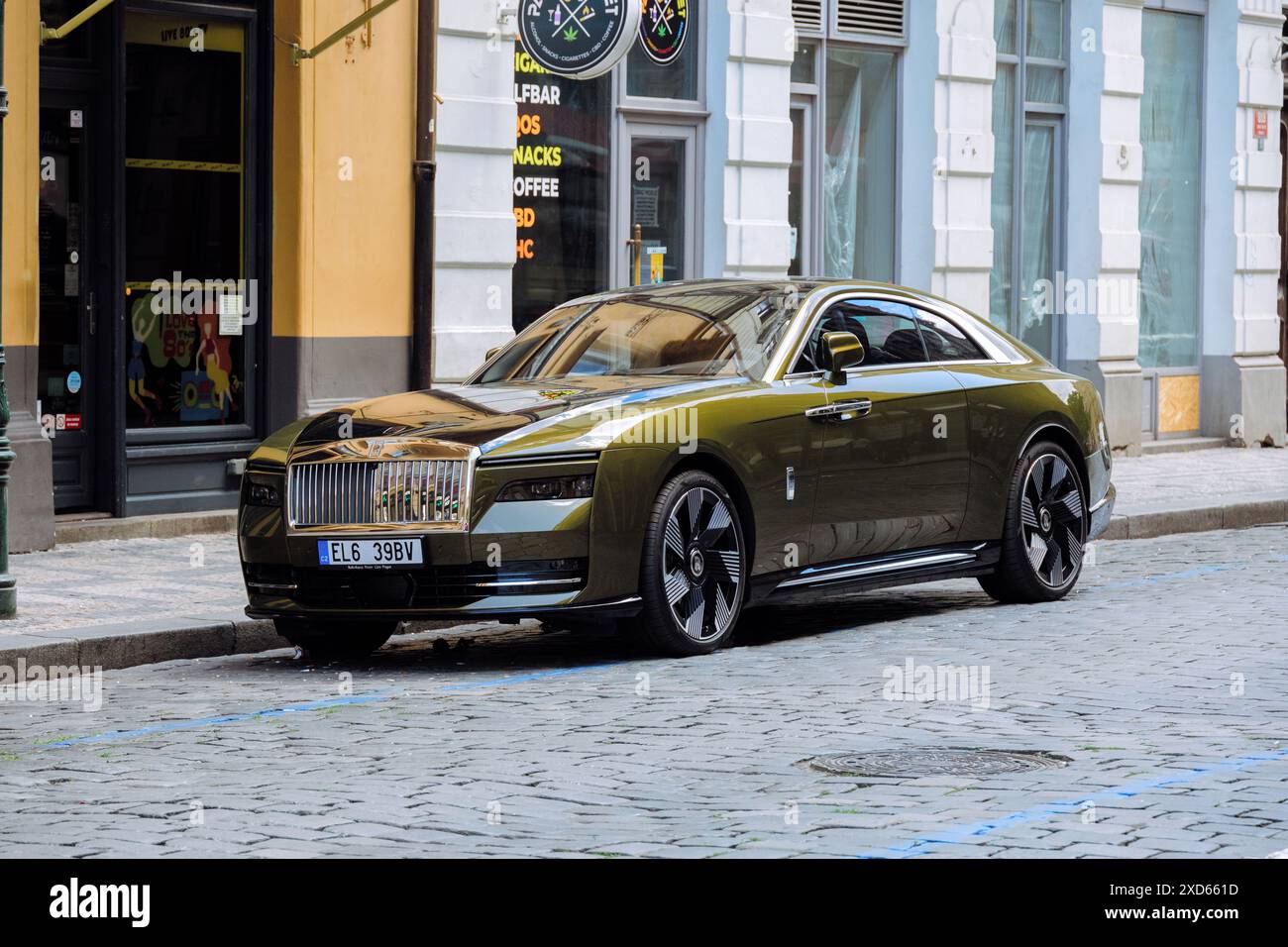 Ein vollständig elektrischer Rolls-Royce Spectre, der auf einer Kopfsteinpflasterstraße im Stadtzentrum von Prag mit historischen Gebäuden und modernen Geschäften im Hintergrund parkt Stockfoto