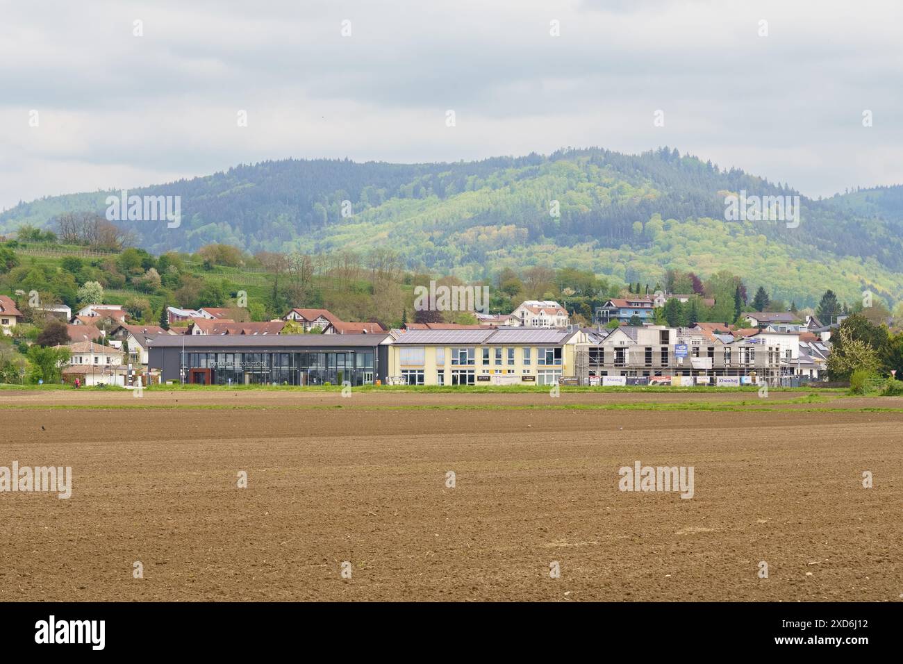 Friesenheim, Deutschland - 29. April 2023: Blick auf ein ländliches Dorf am Fuße einer Bergkette. Die Gebäude sind von einem großen, gepflügten Gebäude umgeben Stockfoto