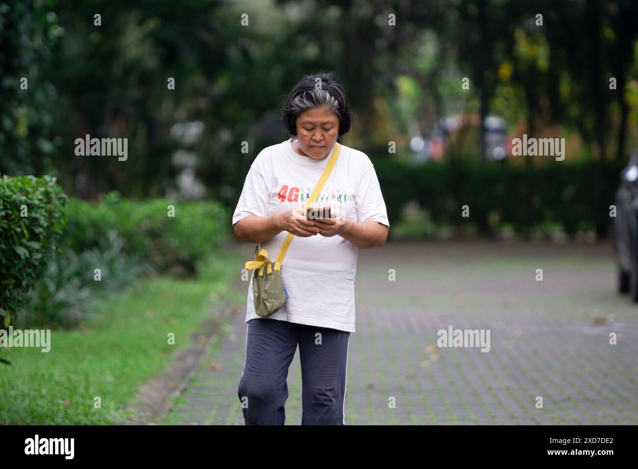 Lässiger Spaziergang einer Frau mittleren Alters mit Telefon auf dem Bürgersteig Stockfoto