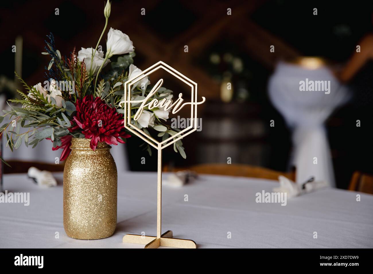 Hochzeitsempfang im Freien - Gäste-Tisch-Einrichtung. Goldene Glitzervase mit burgunderroten Pfingstrosen, Eukalyptusblätter Blumenarrangement Stockfoto