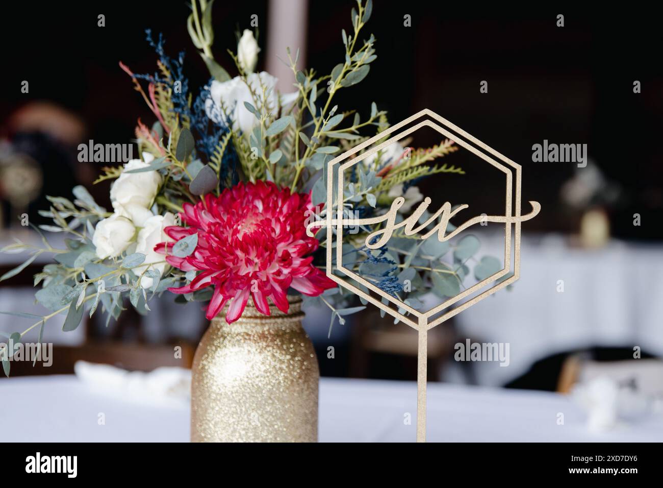 Hochzeitsempfang im Freien - Gäste-Tisch-Einrichtung. Goldene Glitzervase mit burgunderroten Pfingstrosen, Eukalyptusblätter Blumenarrangement Stockfoto
