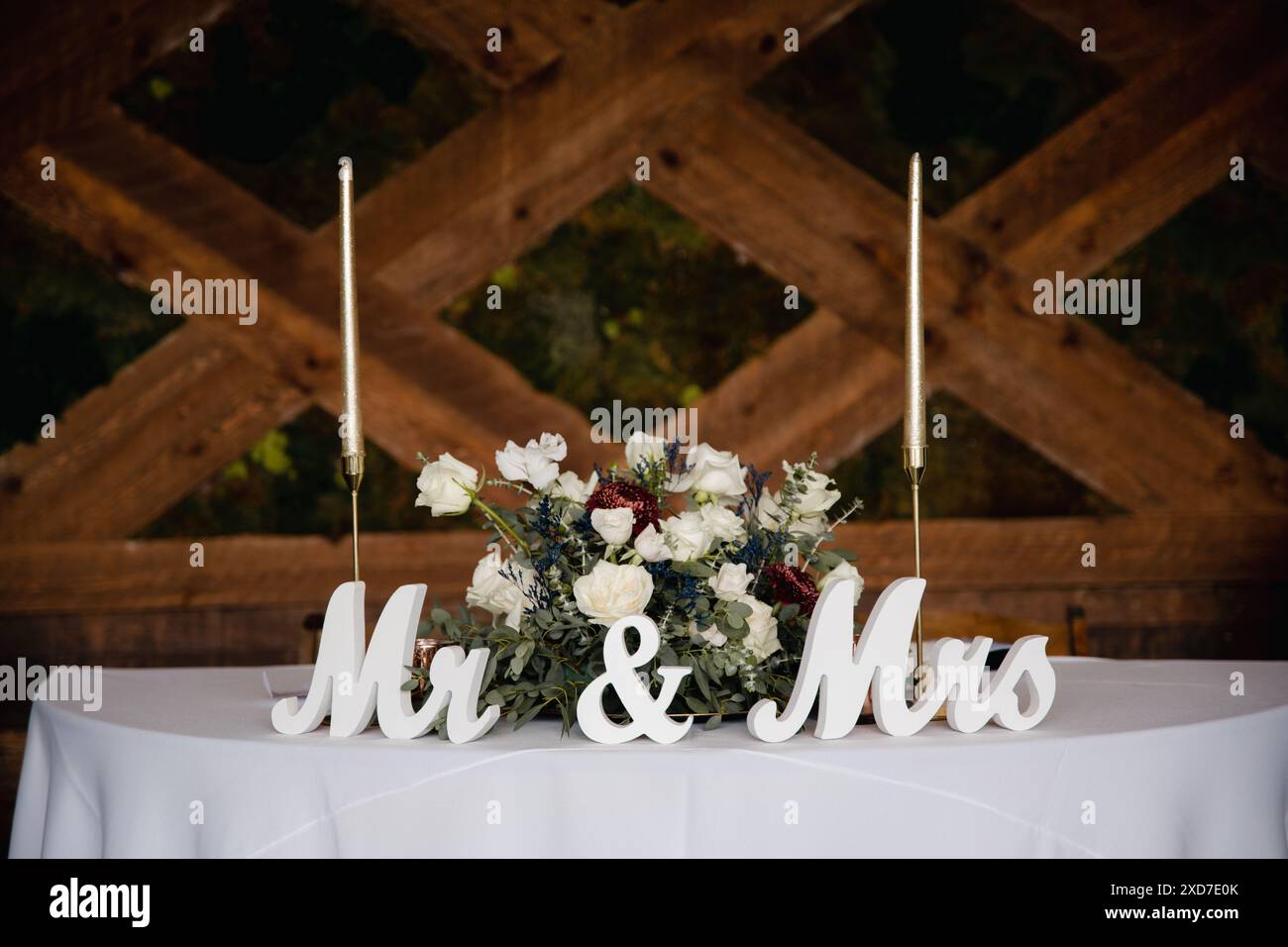 Hochzeitsempfang im Freien - Gäste-Tisch-Einrichtung. Goldene Glitzervase mit burgunderroten Pfingstrosen, Eukalyptusblätter Blumenarrangement Stockfoto