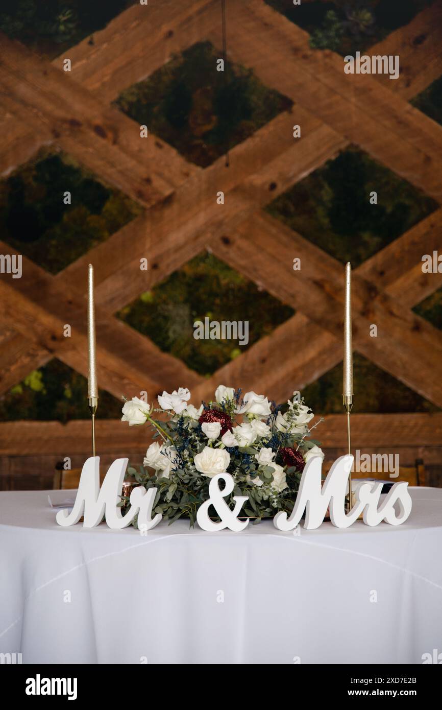Hochzeitsempfang im Freien - Gäste-Tisch-Einrichtung. Goldene Glitzervase mit burgunderroten Pfingstrosen, Eukalyptusblätter Blumenarrangement Stockfoto