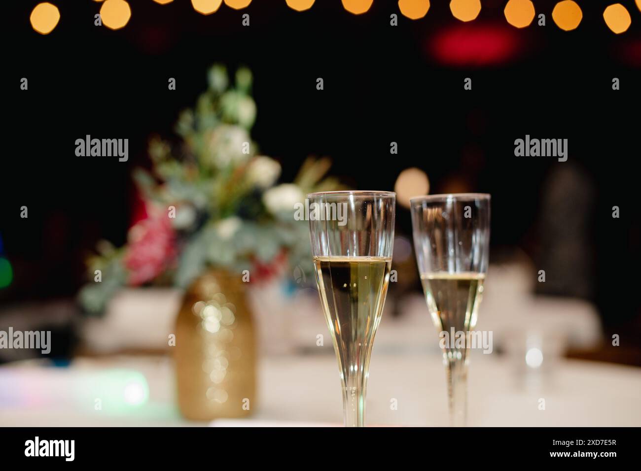 Zwei Champaigne-Flöten auf einem Tisch mit goldglänzender Vase und Blumenarrangements, Lichterketten. Stockfoto