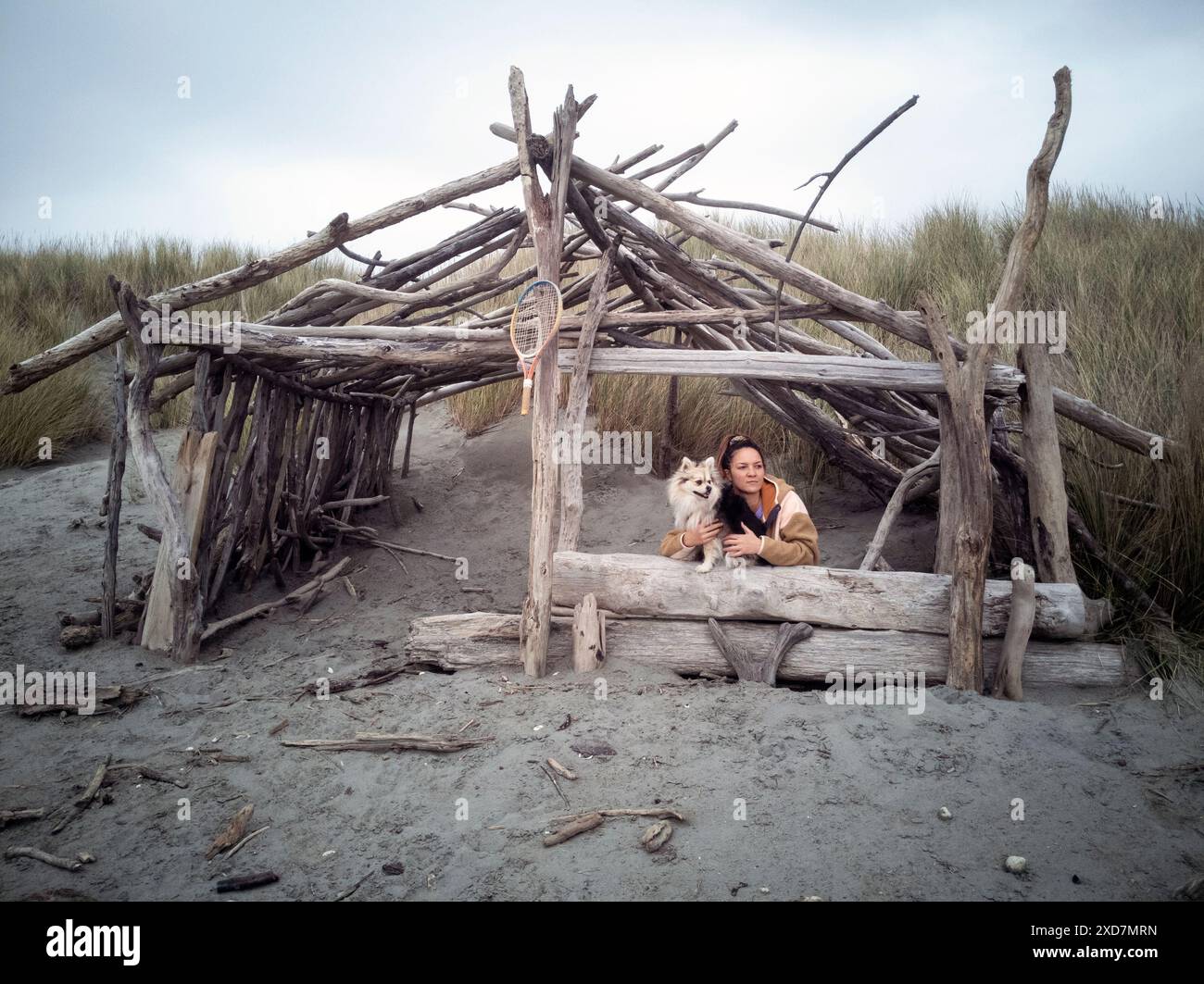 Frau und Hund sitzen in einer Treibholzhütte am Strand in Kapiti, Neuseeland Stockfoto