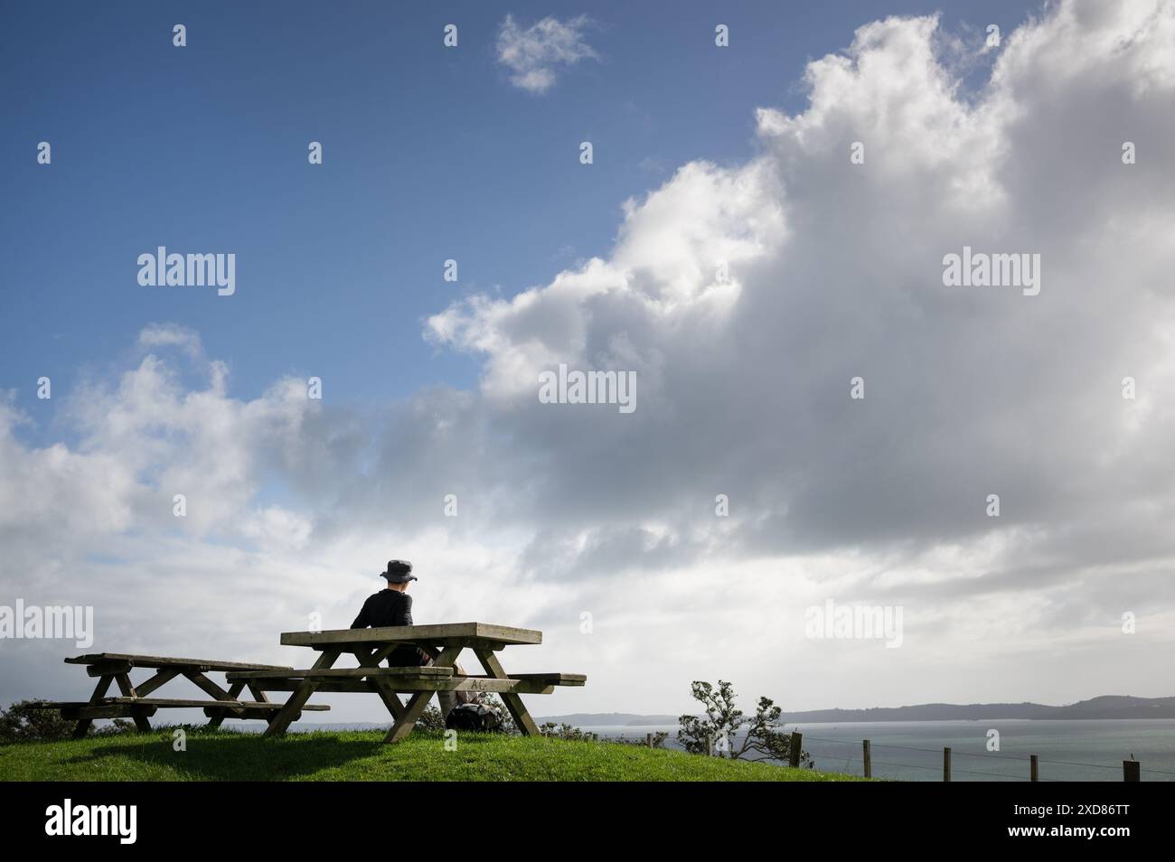 Mann sitzt auf der Picknickbank und genießt die Aussicht. Duder Regional Park. Auckland. Stockfoto