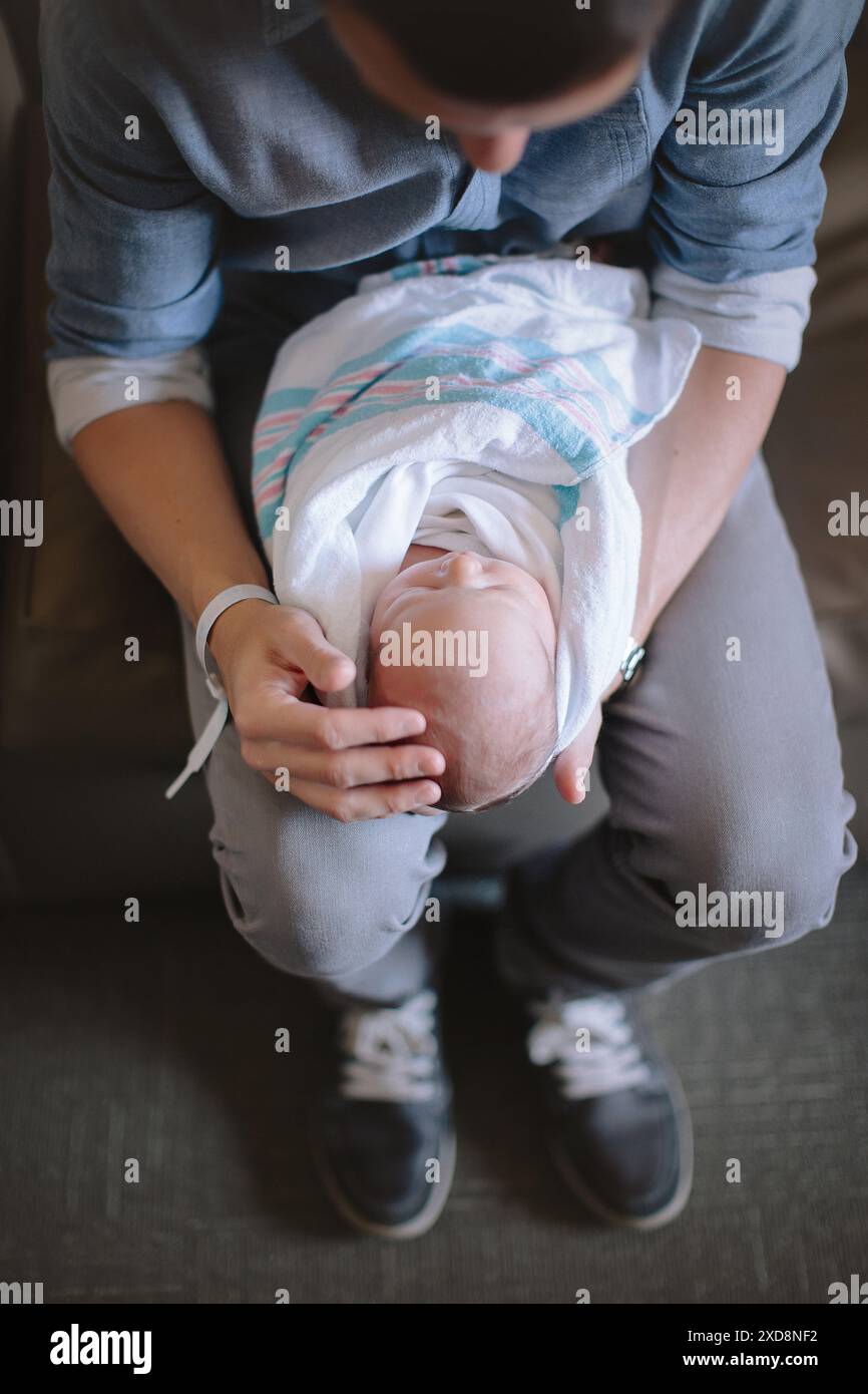 Eine Person, die ein neugeborenes Baby in eine Decke auf dem Schoß legt Stockfoto