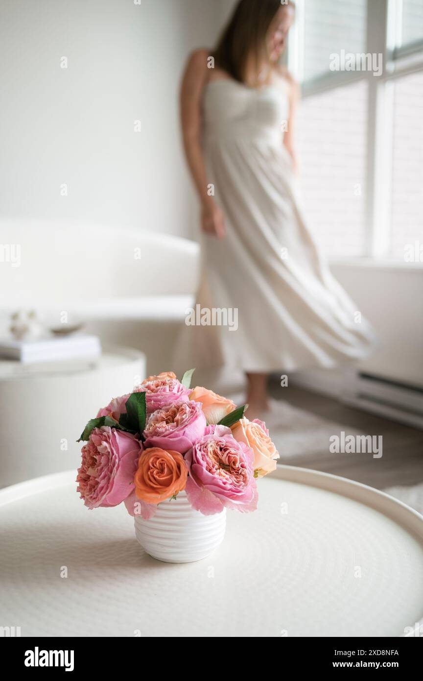 Vase mit rosa und orangen Rosen auf einem Tisch, Frau im Hintergrund. Stockfoto