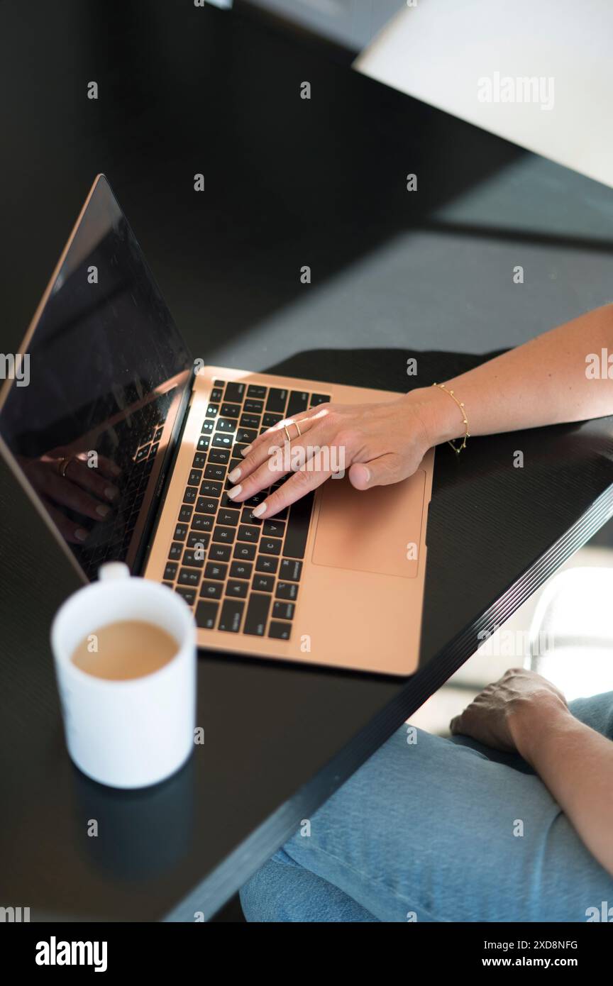 Handtippen auf einem Laptop mit einer Kaffeetasse auf einem schwarzen Schreibtisch. Stockfoto
