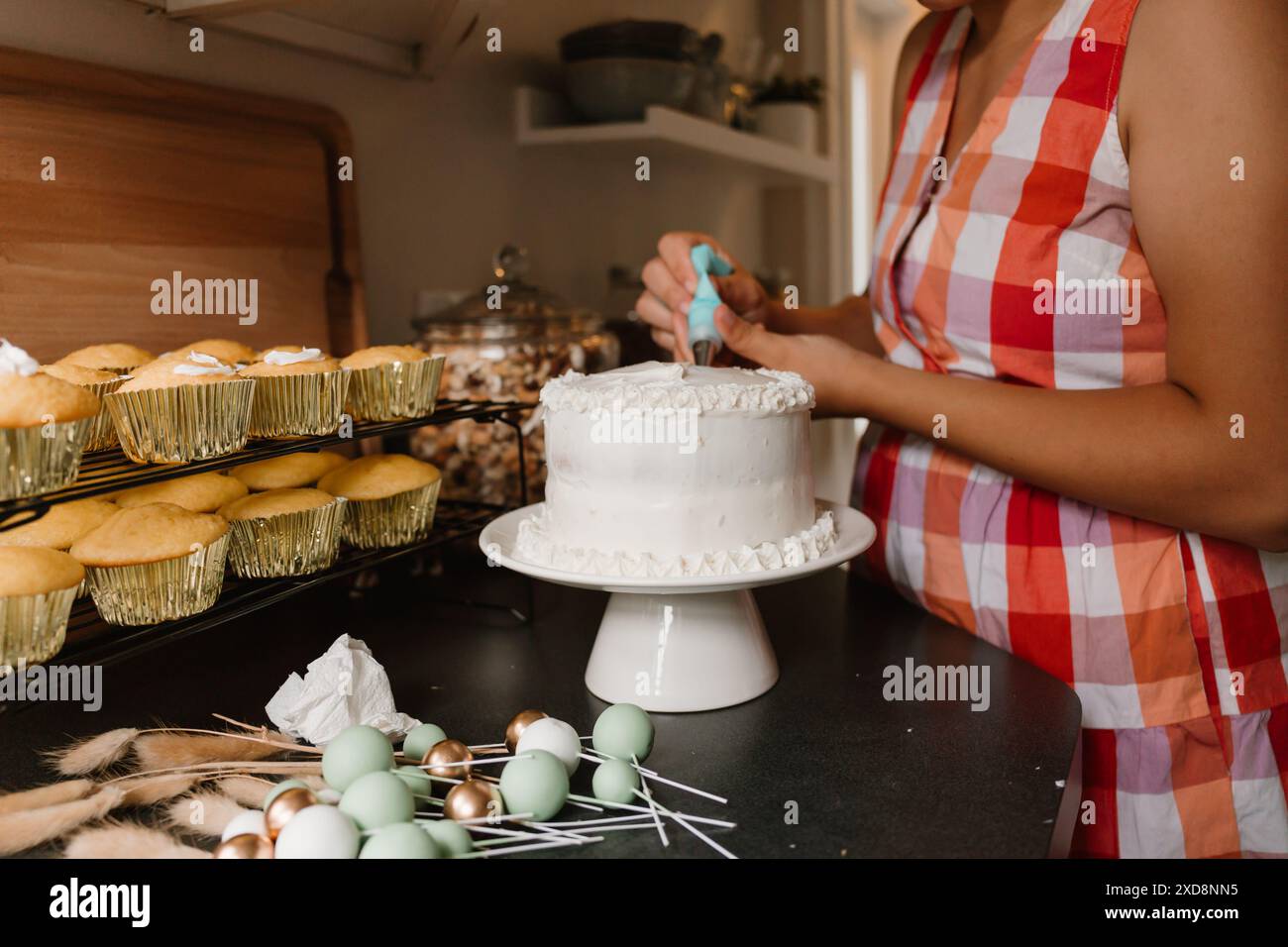 Eine Frau, die einen Geburtstagskuchen mit weißem Zuckerguss dekoriert Stockfoto
