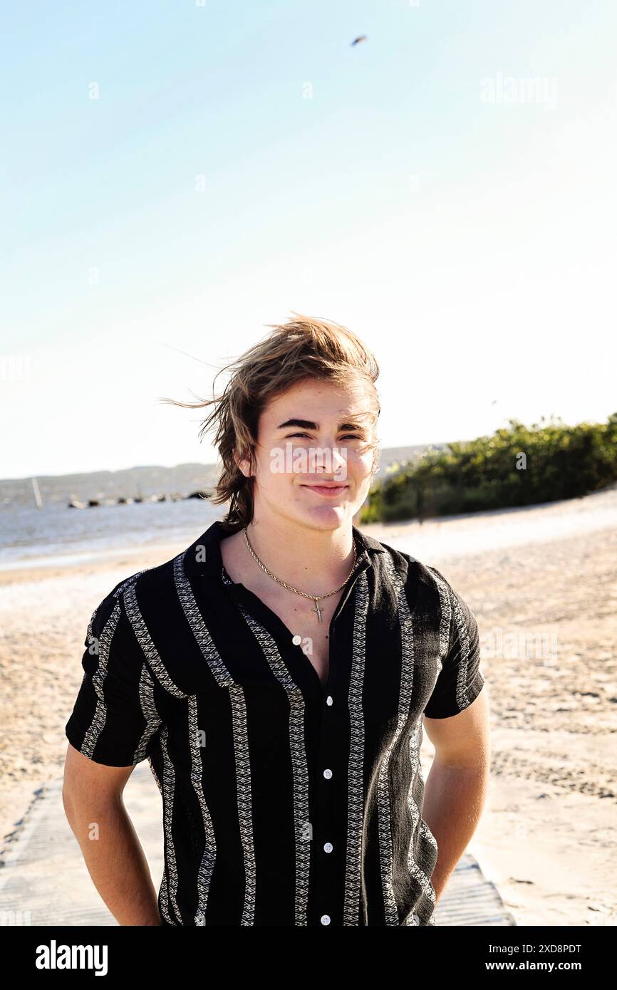 Junger Mann mit einem entspannten Lächeln, der in ungezwungener Atmosphäre am Strand steht Stockfoto