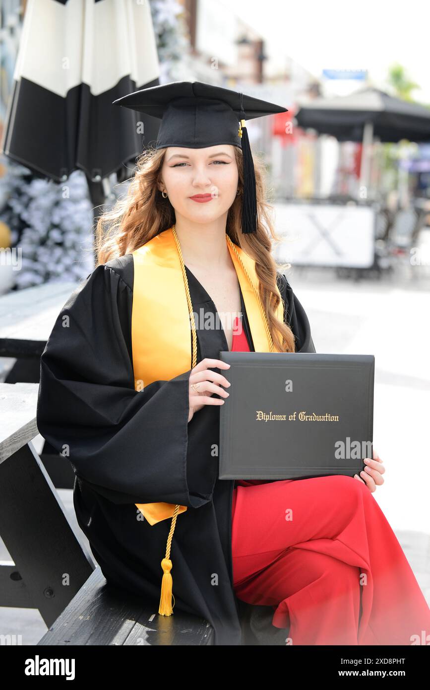 Abschluss in Mütze und Kleid mit Diplom, lächelnd im Freien. Stockfoto