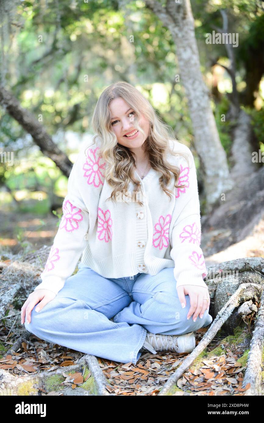 Eine trendige junge Frau mit welligen blonden Haaren, die draußen sitzt, wir Stockfoto