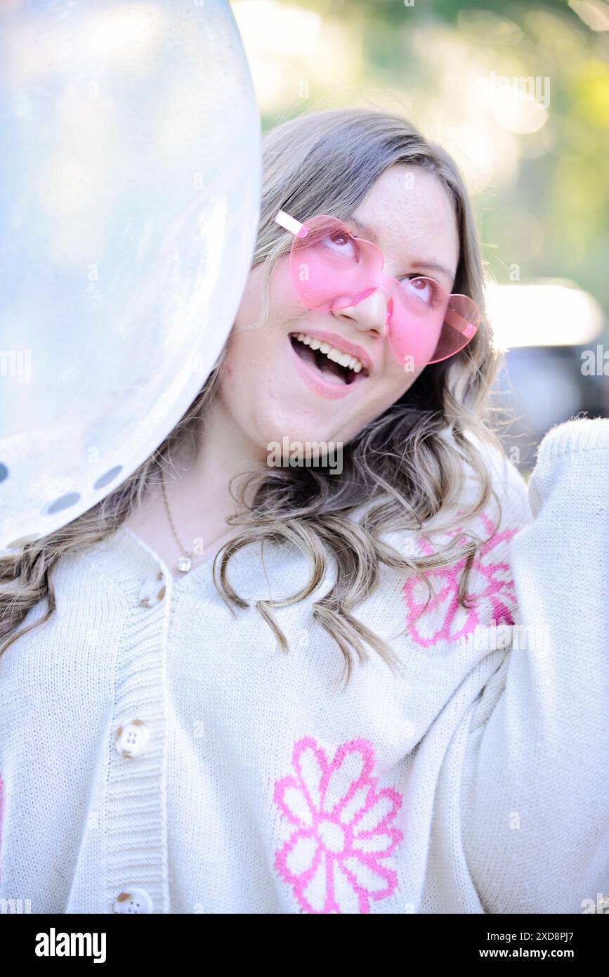 Eine junge Frau mit blonden Haaren trägt eine rosa Sonnenbrille in Herzform Stockfoto