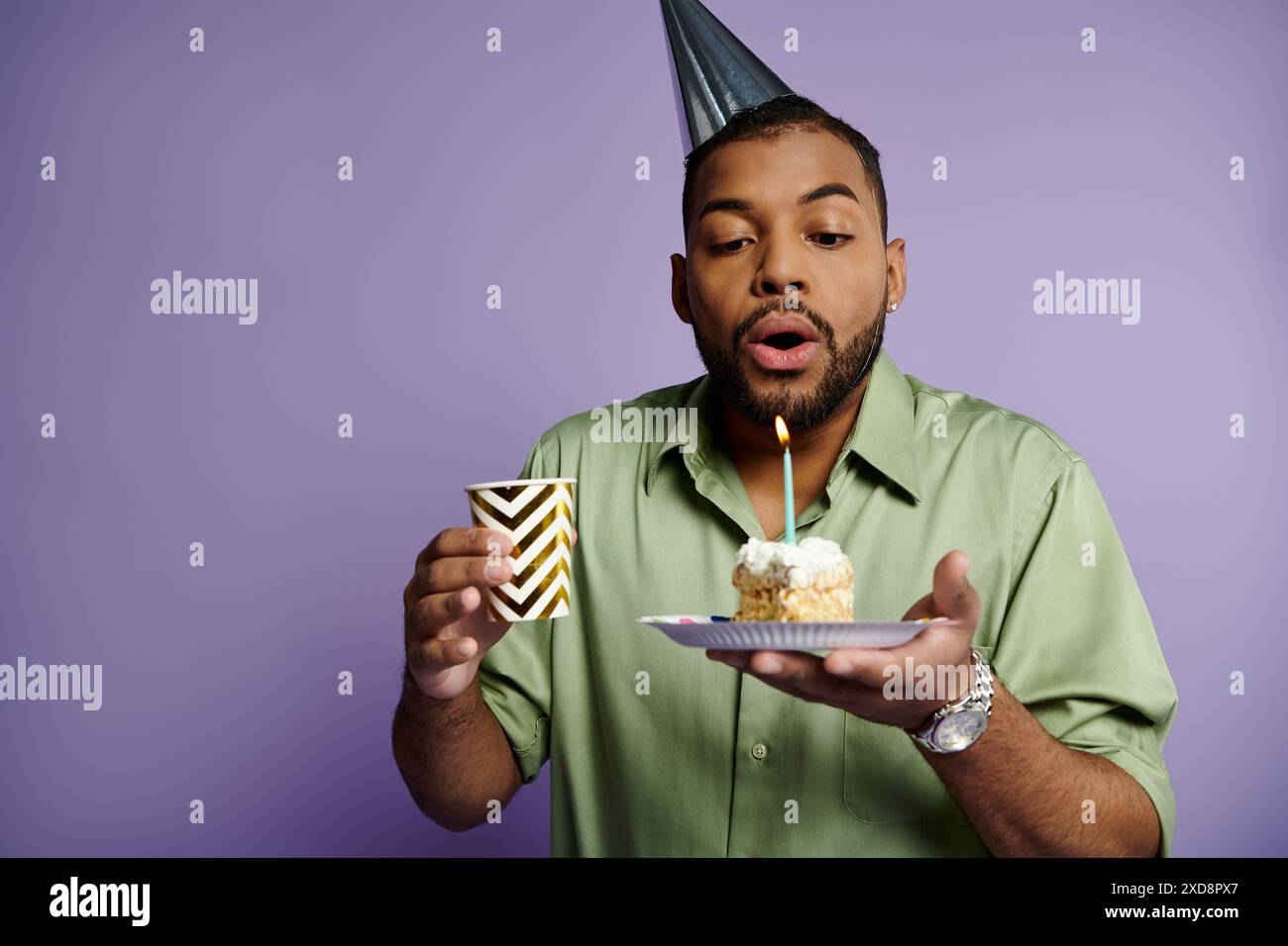 Ein junger afroamerikanischer Mann, der Kerze auf Geburtstagskuchen auf lila Hintergrund bläst. Stockfoto