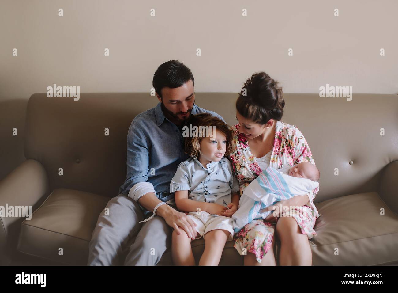 Familie, die mit einem neugeborenen Baby auf einer Couch sitzt, einschließlich eines Mannes, Stockfoto