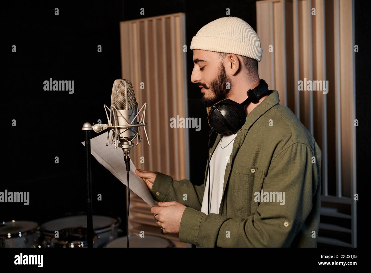 Ein Mann in einem Tonstudio hält ein Blatt Papier und bereitet sich darauf vor, seine Texte in die Probe der Musikbands aufzunehmen. Stockfoto