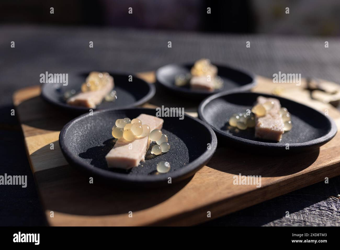 Gourmet-Vorspeisen auf schwarzen Tellern, garniert mit Molekularperlen Stockfoto