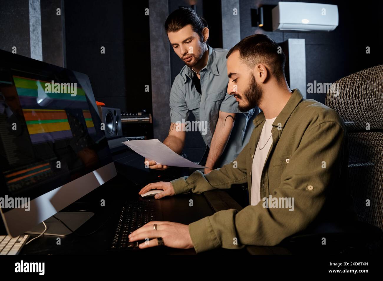Zwei Männer arbeiten an einem Computer in einem Aufnahmestudio zusammen und arbeiten an Musik für ihre Bandprobe. Stockfoto