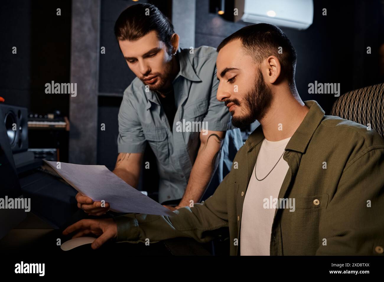 Zwei Männer in einem Tonstudio analysieren sorgfältig ein Notizblatt, tief in Diskussionen. Stockfoto