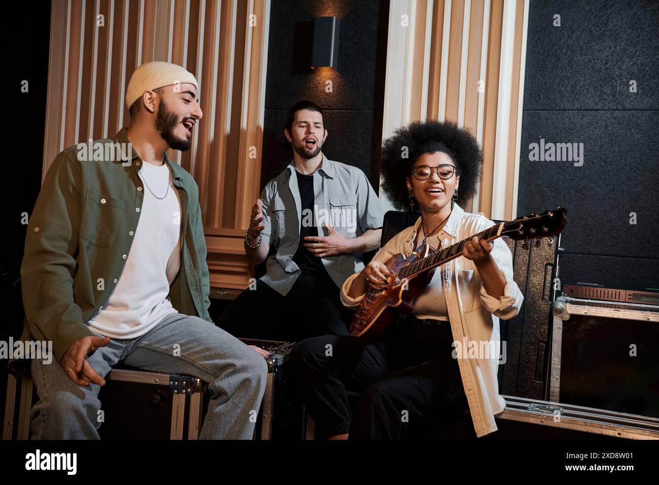 Eine Gruppe von Musikern sitzt in einem Aufnahmestudio, spielt eine Gitarre und arbeitet intensiv mit Musik zusammen. Stockfoto