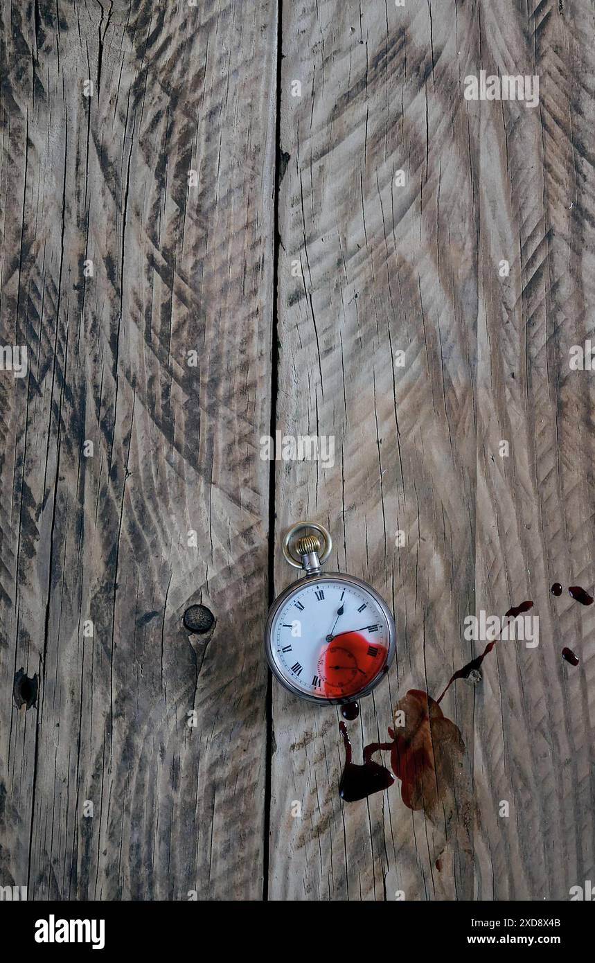 Eine alte Taschenuhr, die auf einem alten Holztisch liegt, mit Blutspritzern darüber. Buchcover Mord Mystery Thriller Stil. Stockfoto