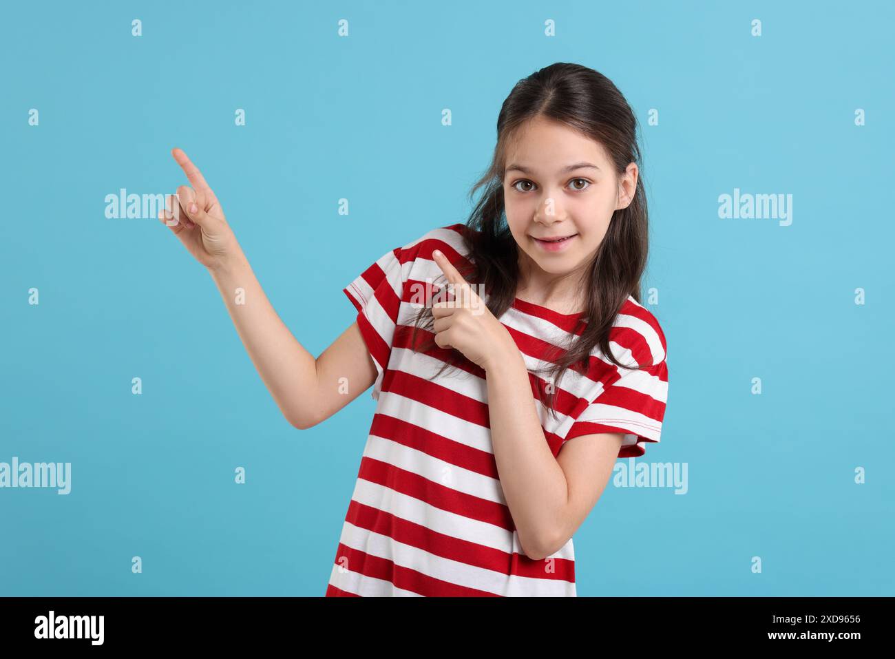 Porträt eines schönen Mädchens, das auf etwas auf hellblauem Hintergrund zeigt Stockfoto