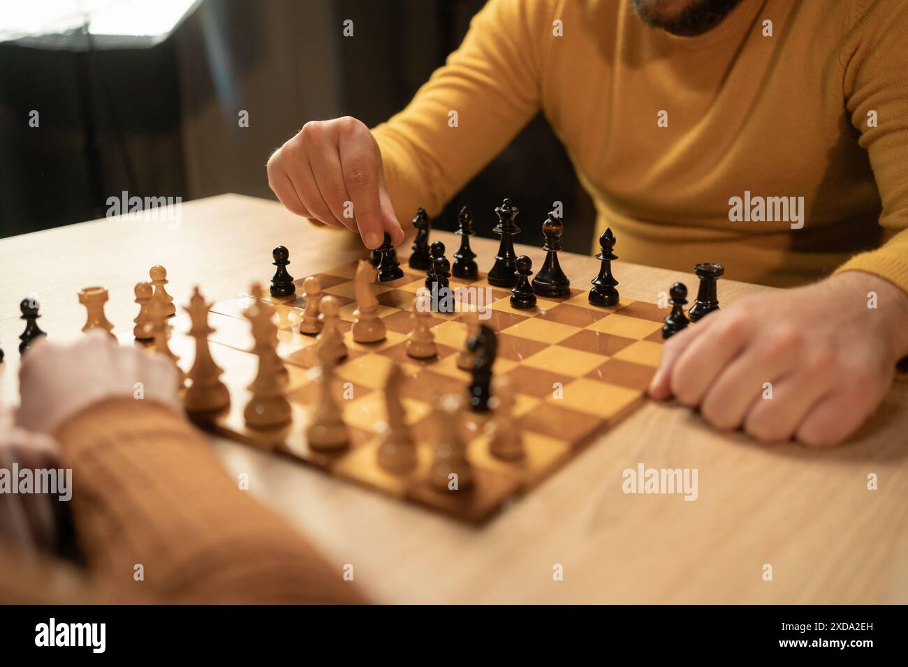 Nahaufnahme zweier Männer, die zu Hause Schach spielen. Der Fokus liegt auf ihren Händen und dem hölzernen Schachbrett, während sie strategische Schritte in einem Innenraum machen Stockfoto