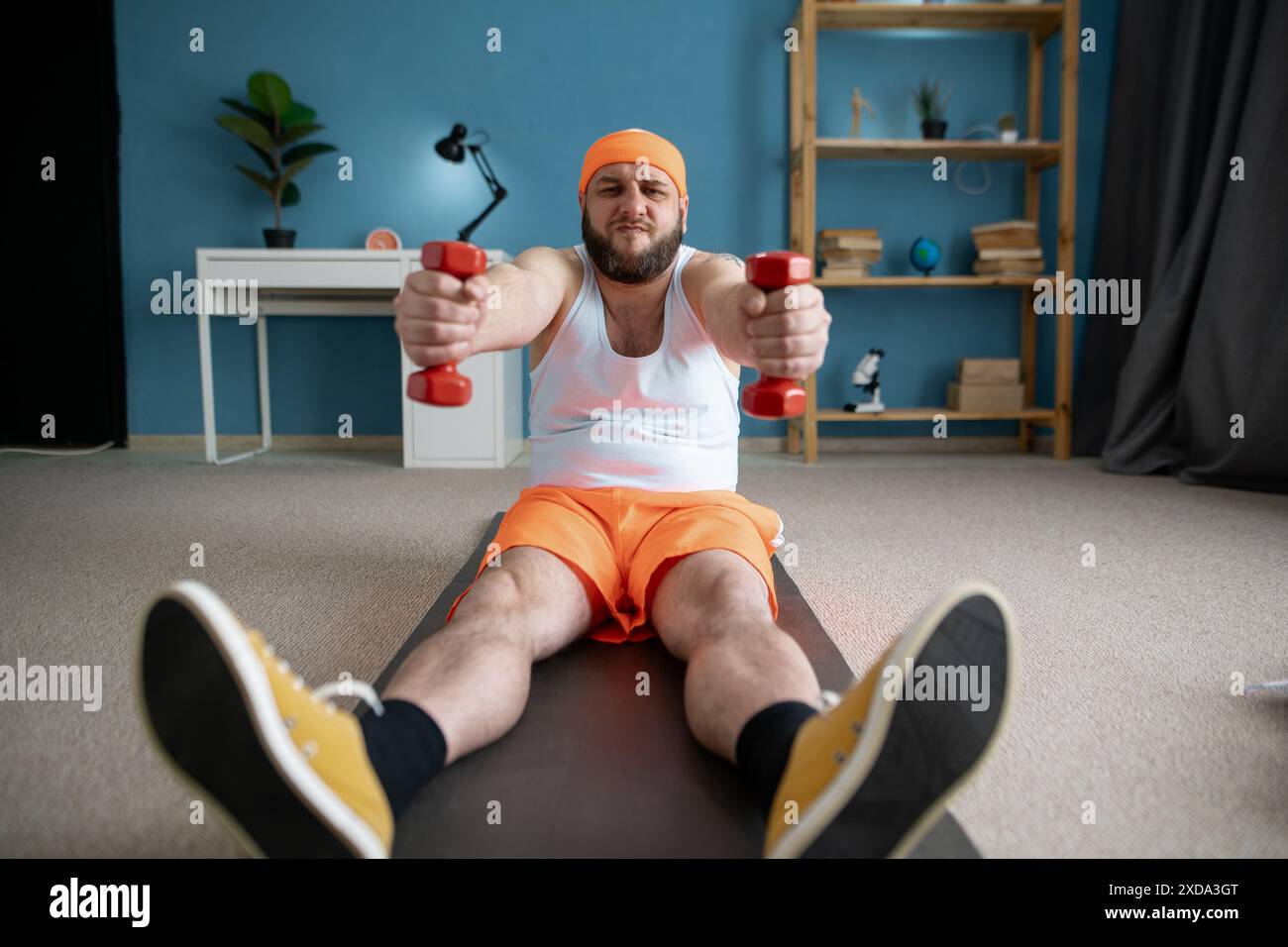 Lustiger Mann in orangen Shorts, der mit kleinen Kurzhanteln trainiert, die Bizepsparodie pumpen. Stockfoto