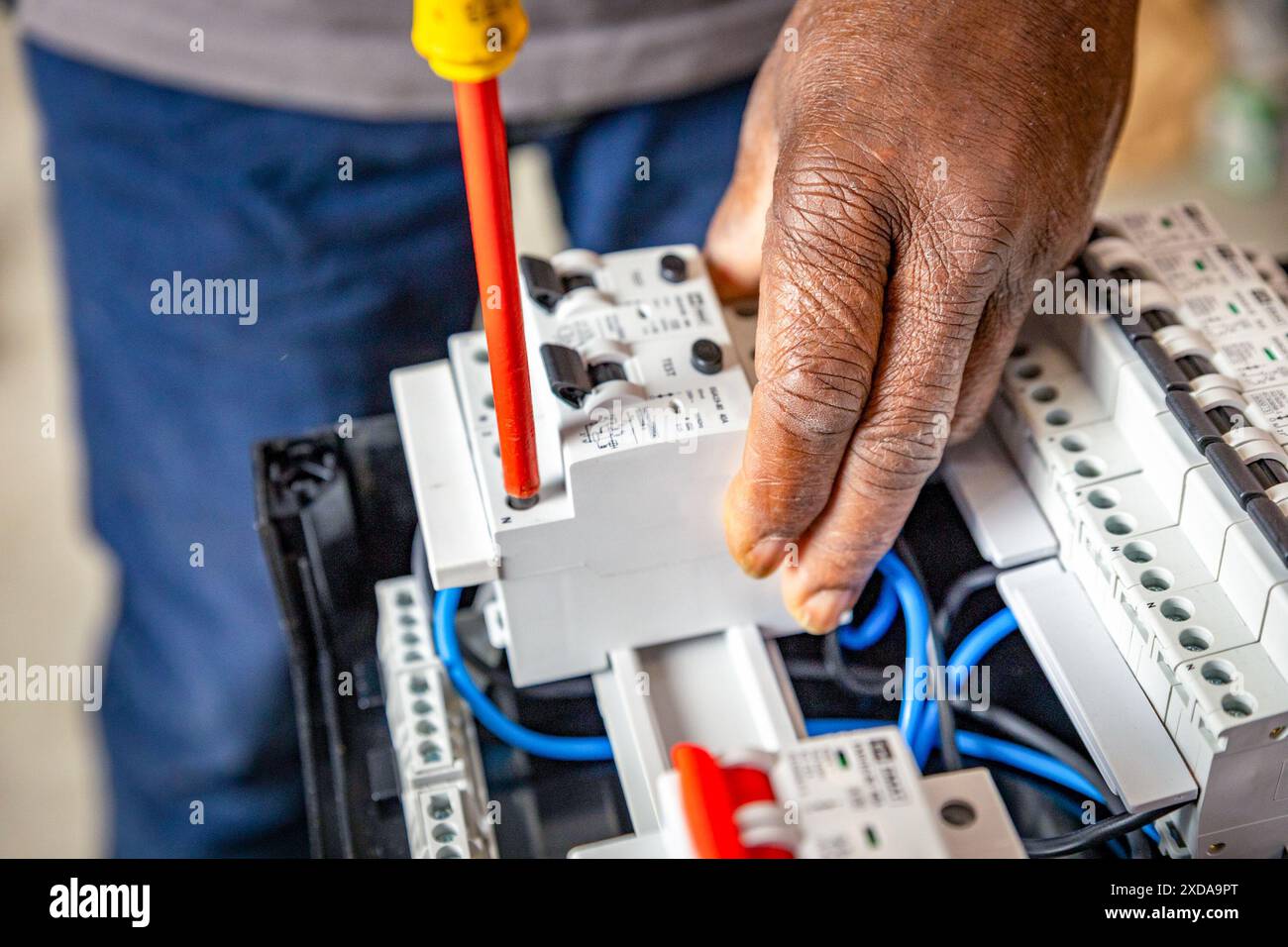 Nahaufnahme eines Elektrikers, der mit einem Schraubendreher an einer Industrietafelmontage arbeitet und neue Kabel an Leistungsschaltern montiert. Stockfoto
