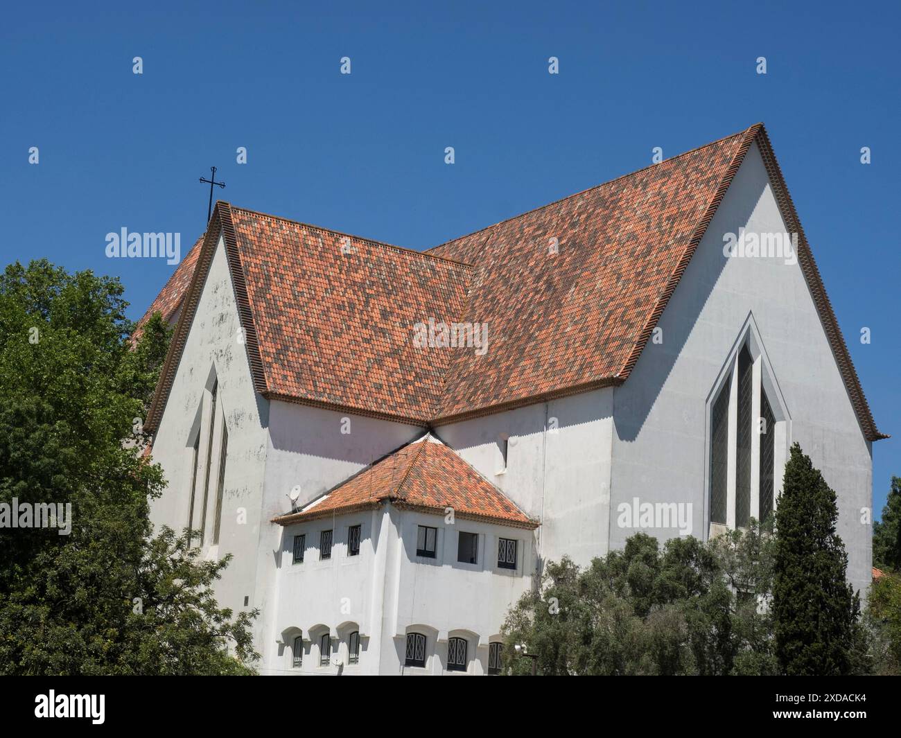 Weiße Kirche mit roten Dachziegeln, umgeben von Bäumen unter blauem Himmel, lissabon, portugal Stockfoto