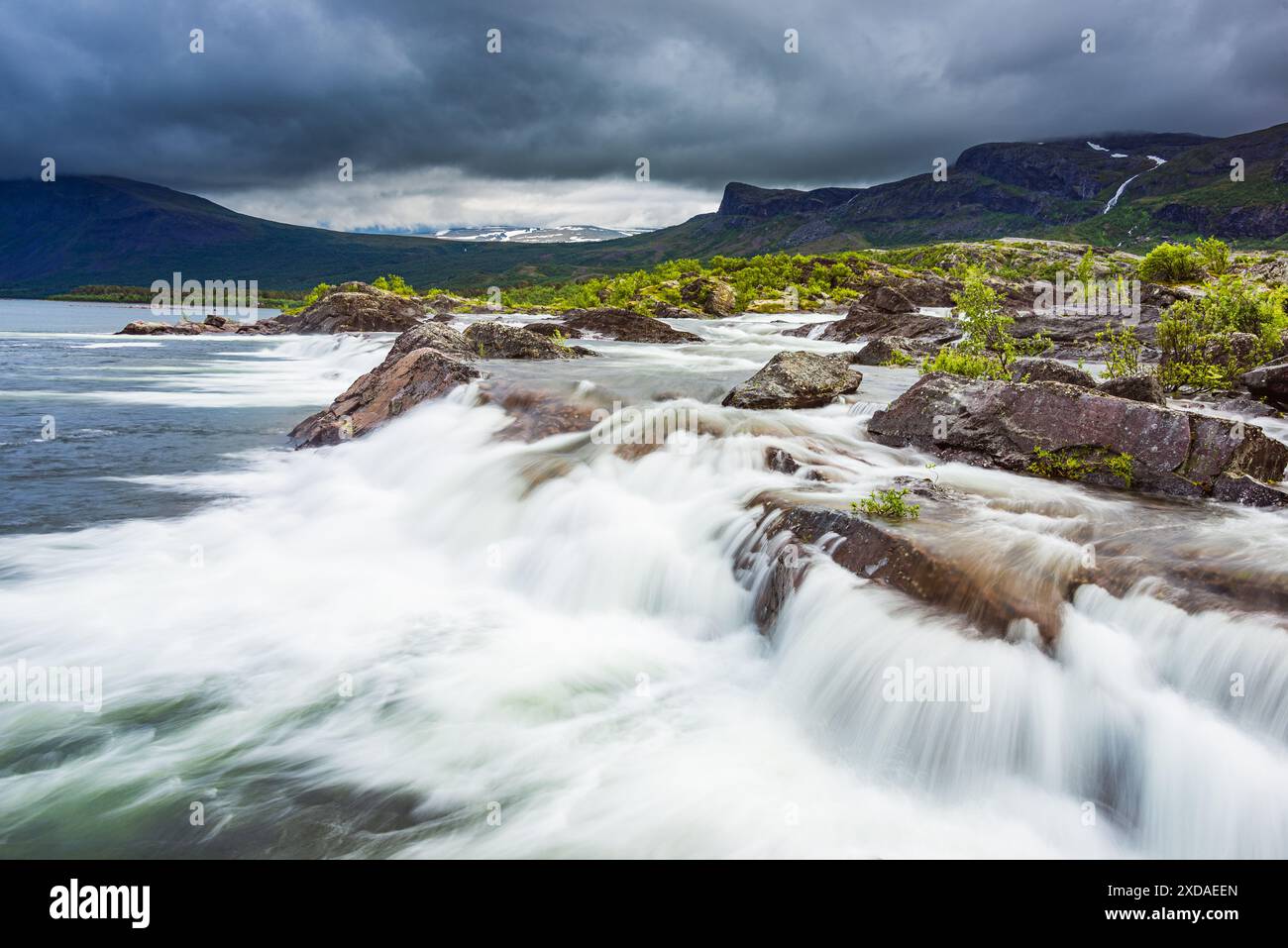 Das Bild zeigt einen atemberaubenden Wasserfall im Stora Sjöfallet Nationalpark in Schweden. Das Wasser fließt über Felsen und kaskadiert in einen See und schafft eine ruhige Atmosphäre Stockfoto