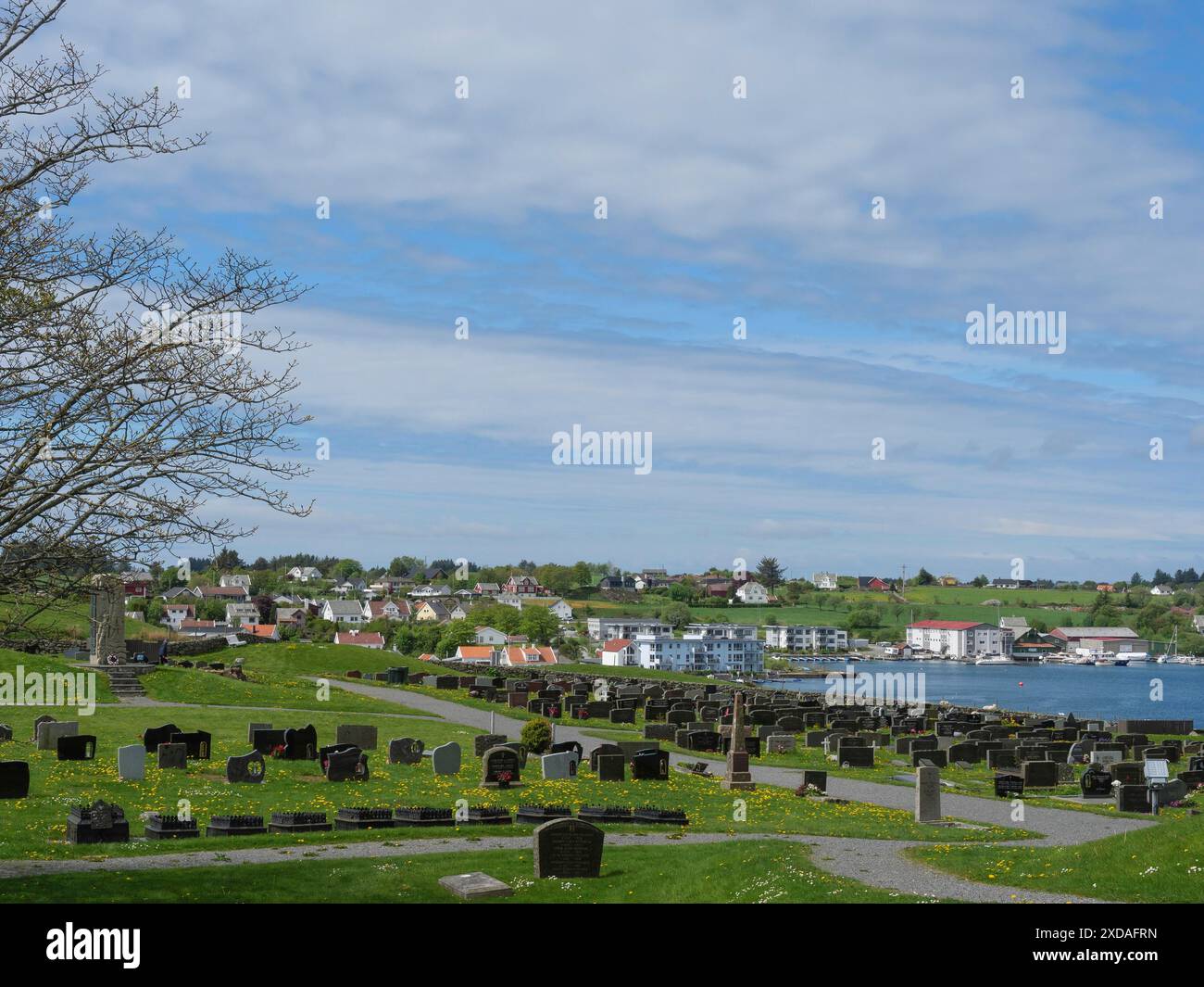 Blick auf einen Friedhof mit Gräbern vor einer weiten Landschaft und einer kleinen Stadt am Meer, haugesund, norwegen Stockfoto