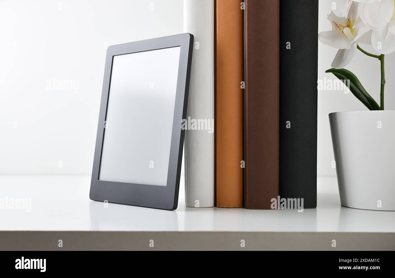 Digitales Lesekonzept mit Bücherregal mit Papierbüchern und darauf anliegendem eBook. Vorderansicht. Stockfoto