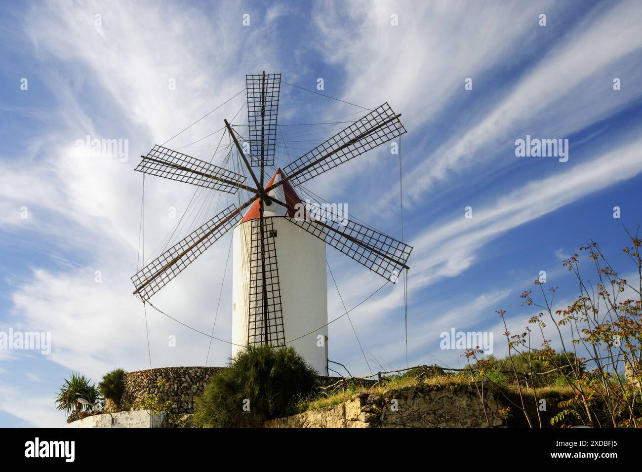 Die San Luis Windmühle auf Menorca steht hoch vor einem leuchtend blauen Himmel mit schimmernden Wolken. Ein historisches Wahrzeichen, das die kulturelle Heldin der Insel widerspiegelt Stockfoto