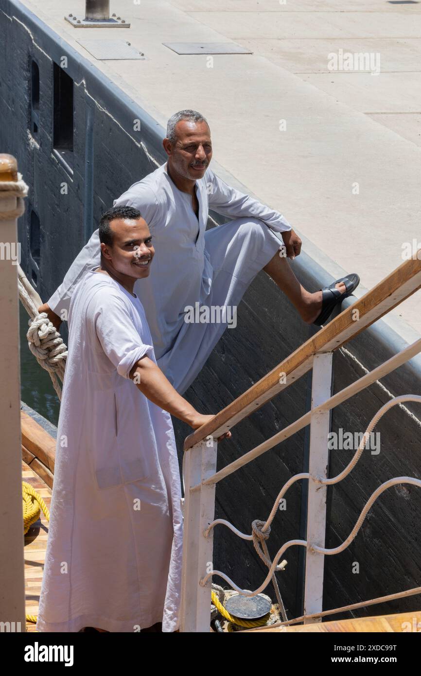 Zwei traditionell gekleidete ägyptische Besatzungsmitglieder eines Lazul Dahabiya Segelbootes warten darauf, dass das Wasser in der Schleuse Esna aufsteigt. Stockfoto