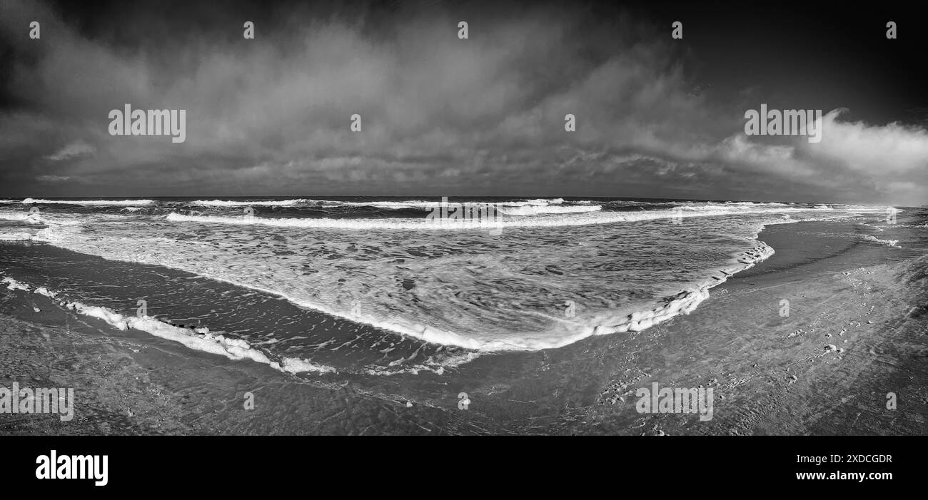 Schwarzweißbild mit Panoramablick auf die Atlantikküste an einem Sommertag. Whitecaps besteigen die blauen Wellen, während sie gegen sie krachen Stockfoto