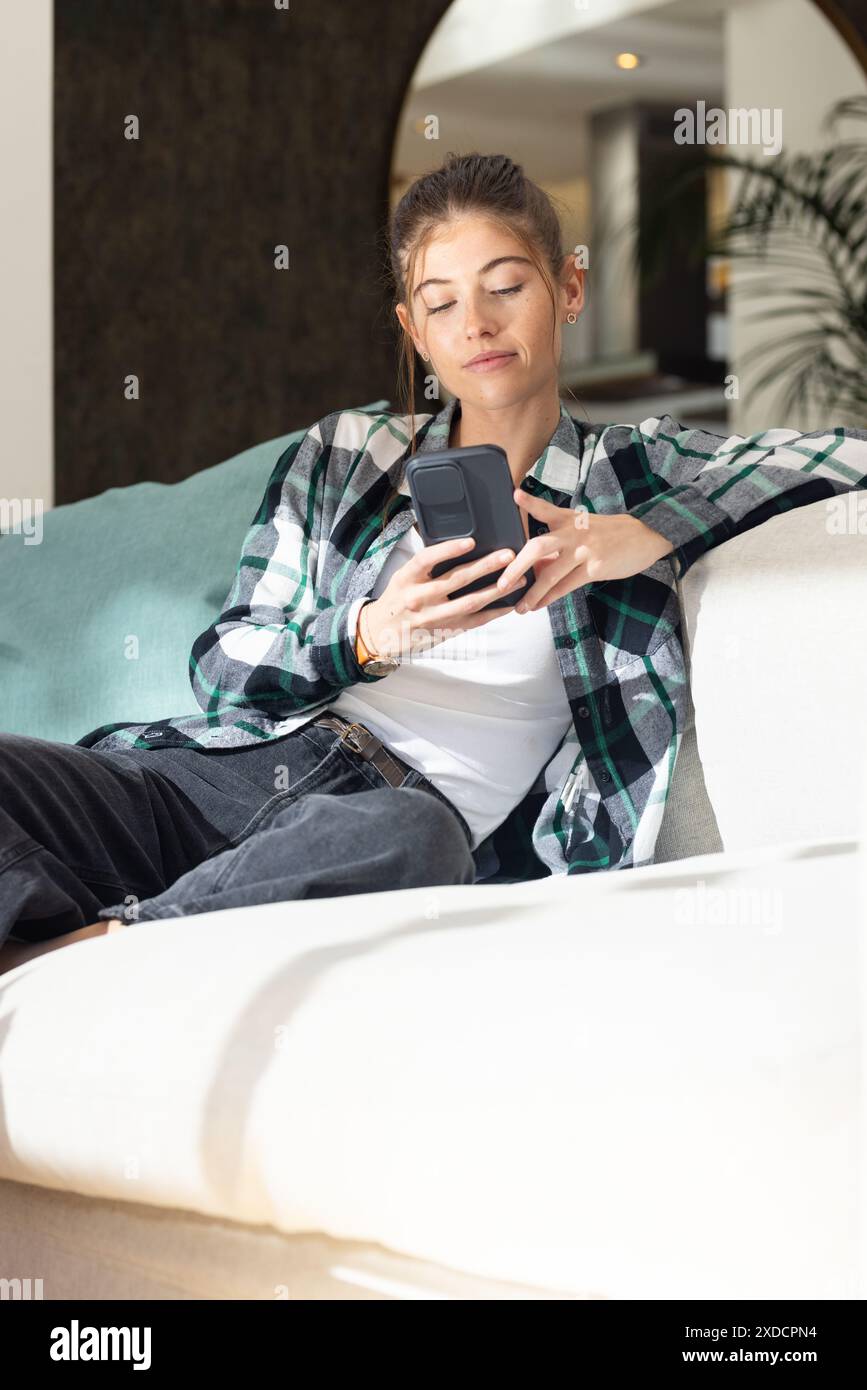 Frau, die sich auf der Couch entspannt, zu Hause auf dem Smartphone scrollt Stockfoto