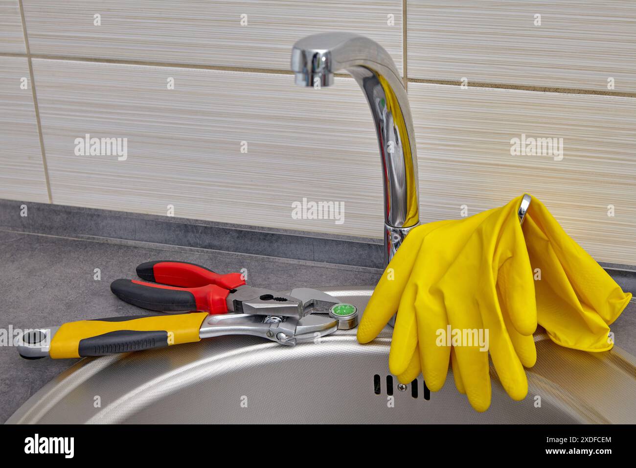 Gelbe Gummihandschuhe und Werkzeuge zum Austausch des Wasserhahnbelüfters für Küchenspüle. Stockfoto