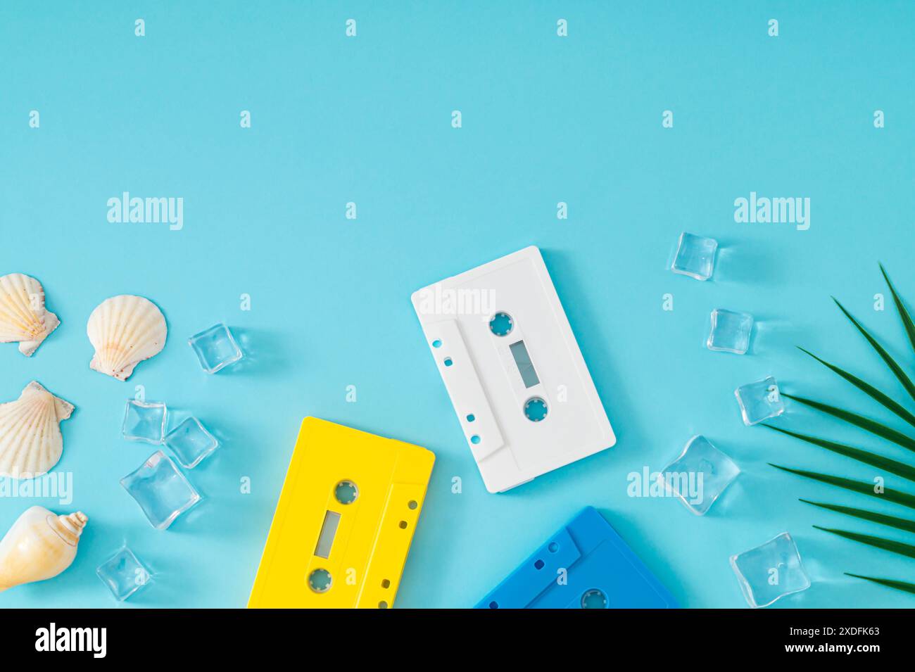 Sommerszene mit Audiokassetten, Muscheln, Eiswürfeln und Palmblatt auf blauem Hintergrund. Sommer-Retro-Musikkonzept. Stockfoto