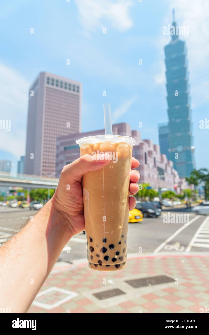 Blick auf die männliche Hand, die traditionellen taiwanesischen Bubble Milk Tee in der Innenstadt von Taipei, Taiwan, hält. Der Wolkenkratzer ist im Hintergrund sichtbar. Stockfoto