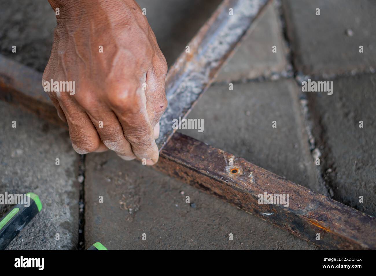 Nahaufnahme einer Person, die an einem rostigen Metallrahmen arbeitet, möglicherweise repariert oder montiert. Die Hand hält ein Werkzeug und es gibt ein sichtbares Schild Stockfoto