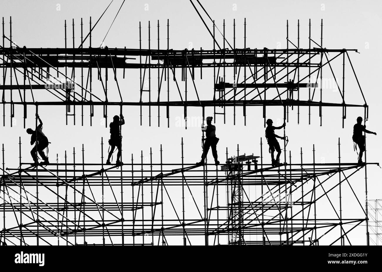 Die Silhouette von Bauarbeitern, die Teamarbeit und Geschicklichkeit nutzen, um einen Stahlturm für ein Unterhaltungs-Festival zusammenzustellen Stockfoto